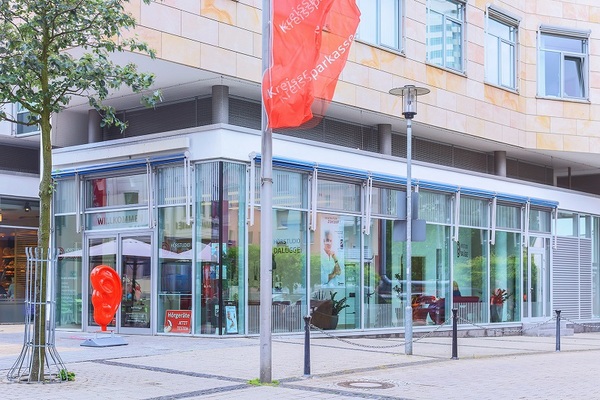 Moderne Filiale der Kreissparkasse mit Glasfassade, roter Flagge und großem Ohr-Symbol.
