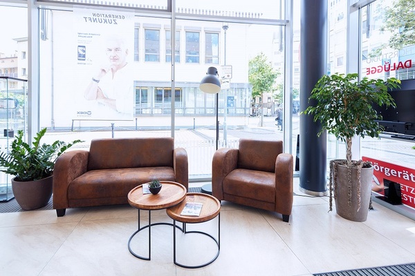 Moderne Wartebereich-Lounge mit braunen Ledersesseln, Couchtischen und großen Pflanzen.