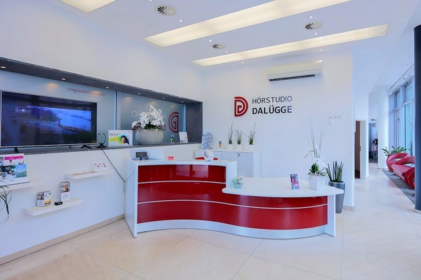 Modernes Empfangsbereich im Hörstudio Dalügge mit rotem Tresen und heller Einrichtung.